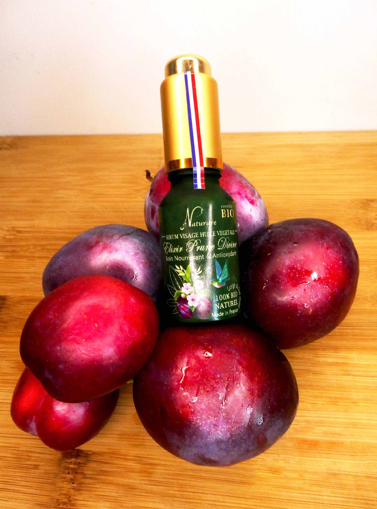 Agnès' Petit Paris Skincare organic plum facial serum bottle surrounded by fresh plums on wooden surface