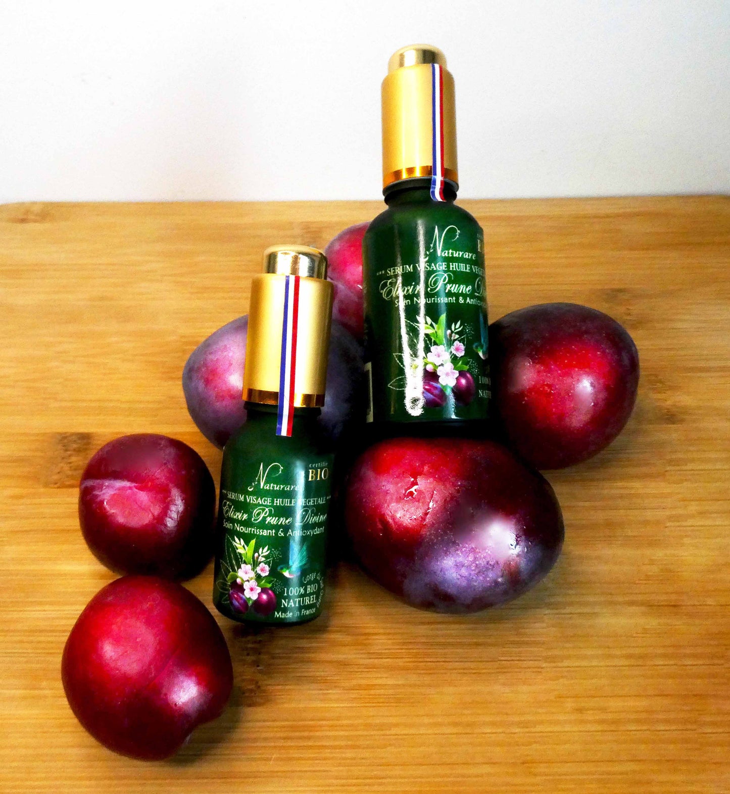 Agnès' Petit Paris Skincare organic plum facial serum bottles with fresh plums on wooden surface