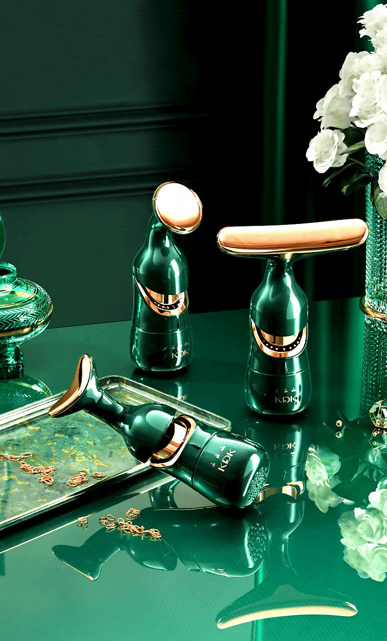 Agnès Petit Paris Delphy-triple head facial massager in green with gold accents on a reflective surface with white flowers