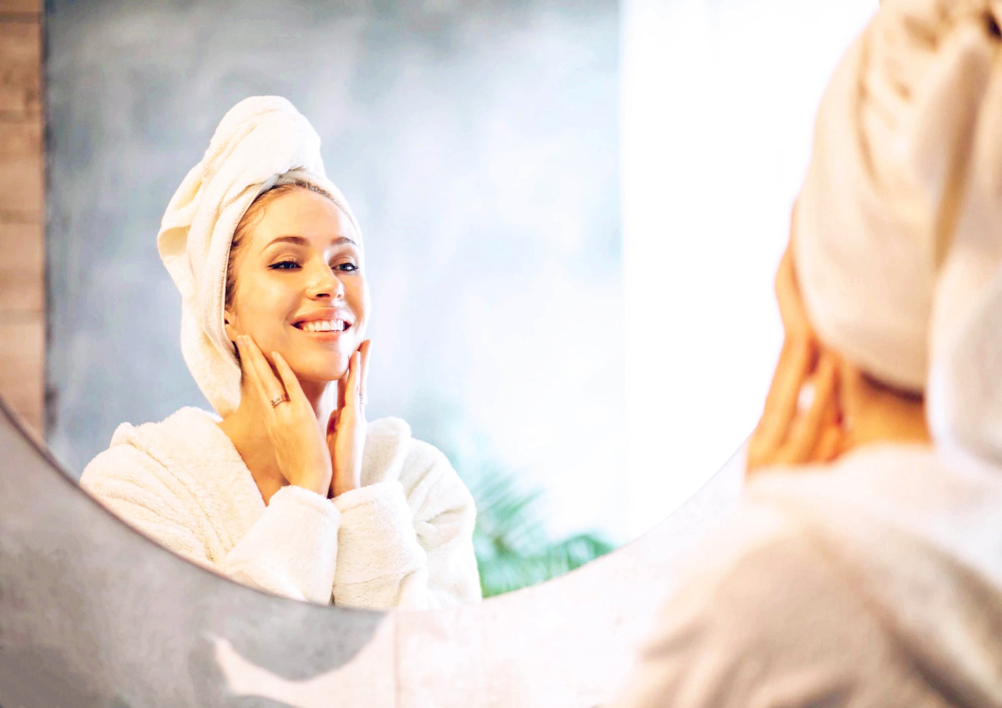 Smiling woman with towel on head applying French natural skincare elixir anti-aging serum in front of mirror